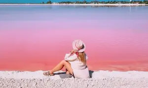 Kobieta w kapeluszu siedzi na piasku, podziwiając niezwykłą, różową plażę w Meksyku.