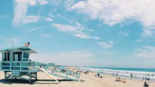 Słoneczna plaża w USA z wieżą ratowniczą i ludźmi odpoczywającymi nad oceanem. Idealne miejsce, by sprawdzić, ile trwają wakacje w USA.