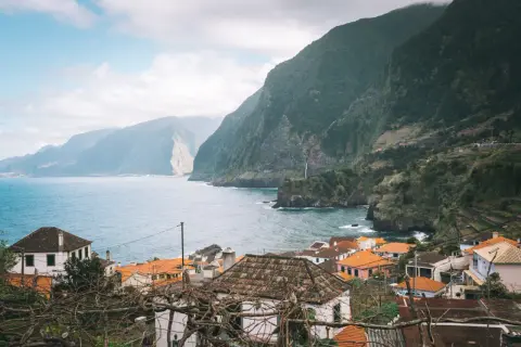 Wiosenna pogoda na Maderze. Wioska z pomarańczowymi dachami u podnóża zielonych gór, z widokiem na ocean.