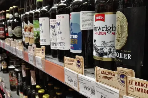 Rząd butelek piwa na półce sklepowej, niektóre z etykietami w języku ukraińskim, sugerującymi import. Widać ceny i nazwy piw, np. "Thwaites Wainwright Golden Ale".