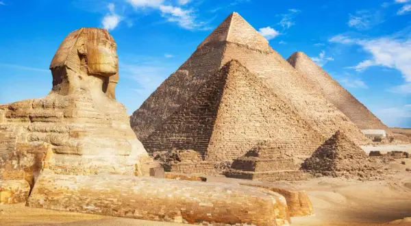 Sfinks i piramidy w Gizie na tle błękitnego nieba z chmurami.