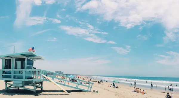 Słoneczna plaża w USA z wieżą ratowniczą i ludźmi odpoczywającymi nad oceanem. Idealne miejsce, by sprawdzić, ile trwają wakacje w USA.