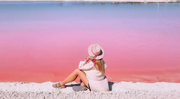 Kobieta w kapeluszu siedzi na piasku, podziwiając niezwykłą, różową plażę w Meksyku.