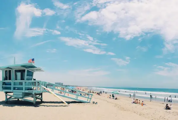 Słoneczna plaża w USA z wieżą ratowniczą i ludźmi odpoczywającymi nad oceanem. Idealne miejsce, by sprawdzić, ile trwają wakacje w USA.